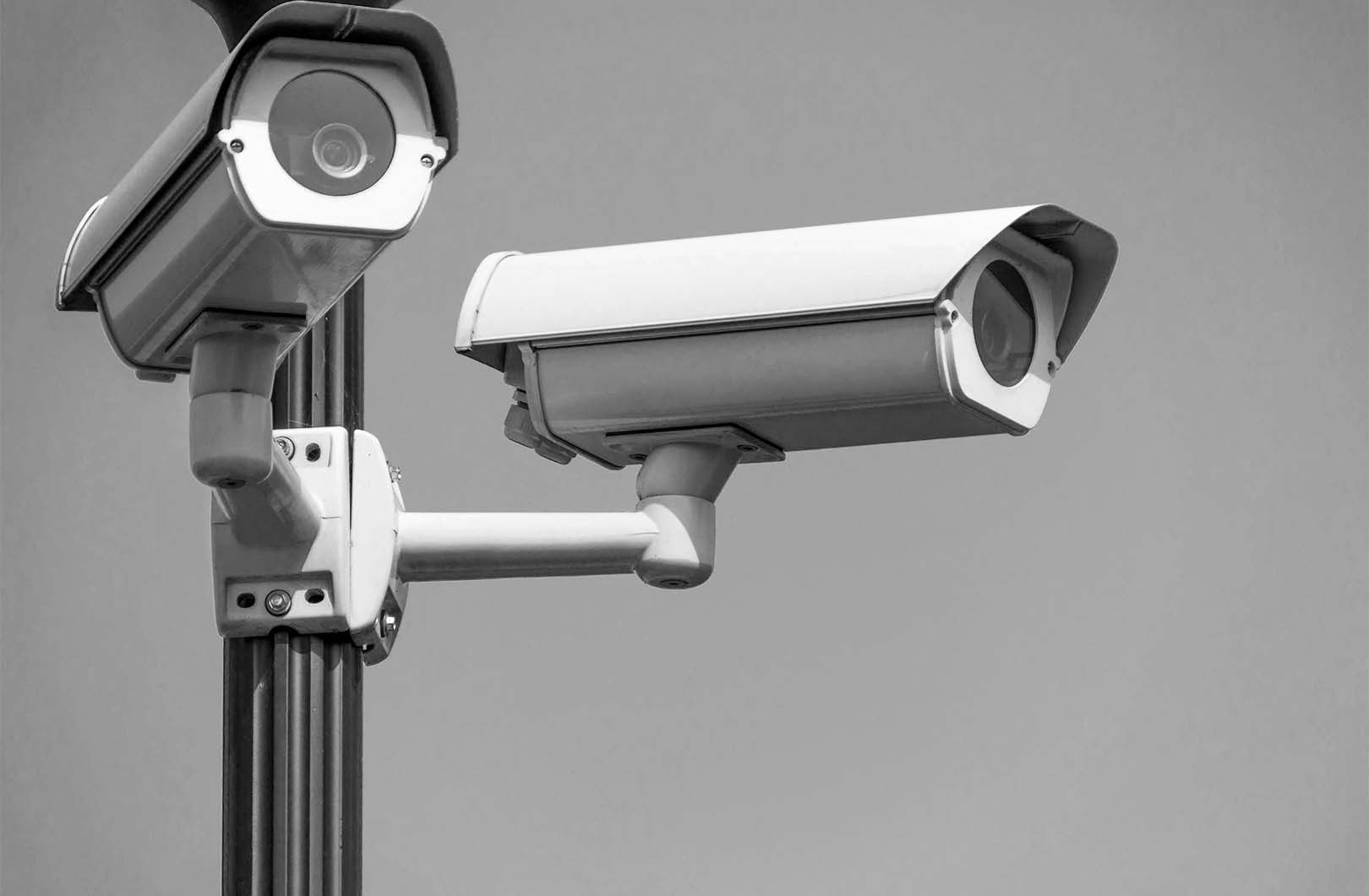 An image of a security camera mounted on a pole or wall, set against a clear sky background, suggesting outdoor surveillance.