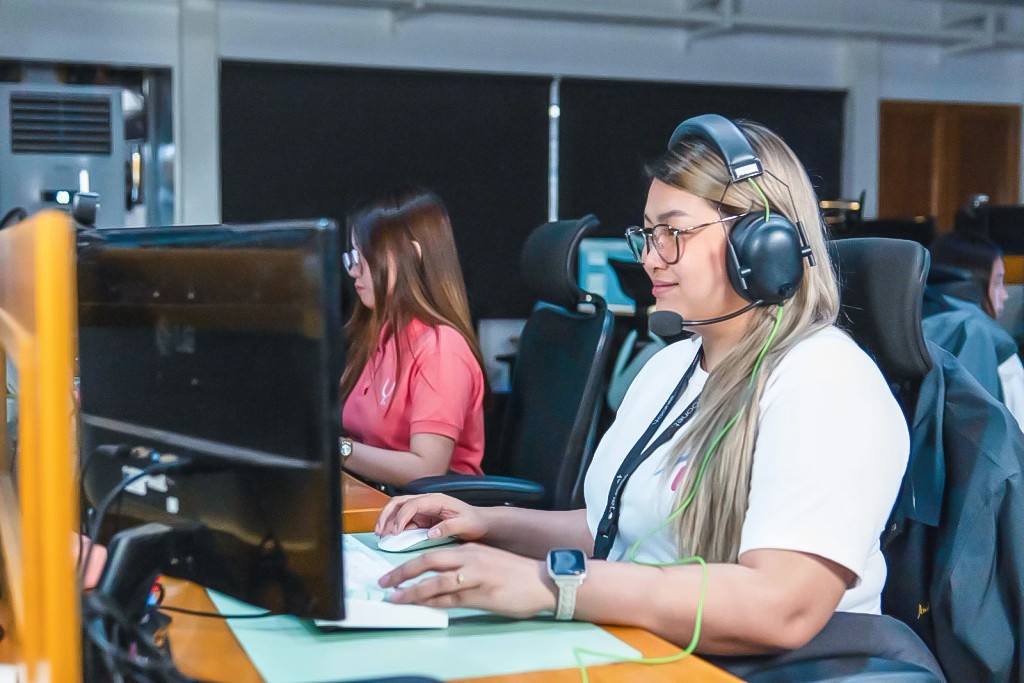 Several employees work at their desks in a busy call center, with headsets on and focused expressions.