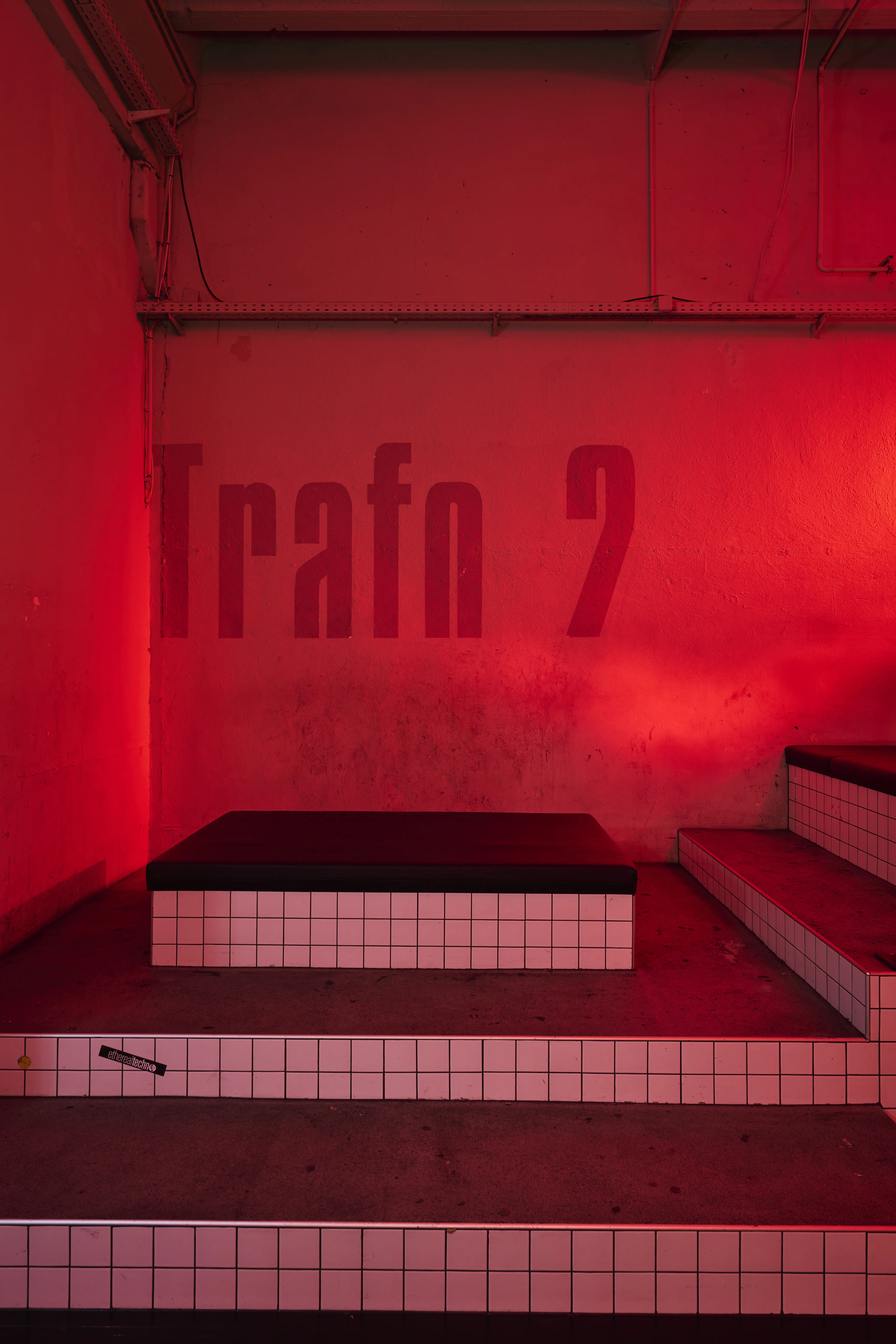 Red-lit corner at TRESOR GLOBUS labelled Trafo 2 in large letters, with stepped white-tiled platforms topped by black seat cushions.