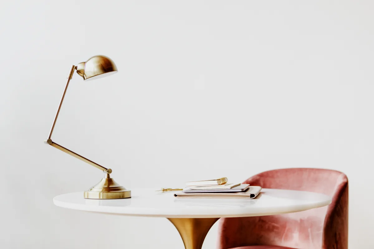 Détail de décoration intérieure avec lampe de bureau en laiton doré sur table ronde en marbre blanc et fauteuil en velours rose poudré