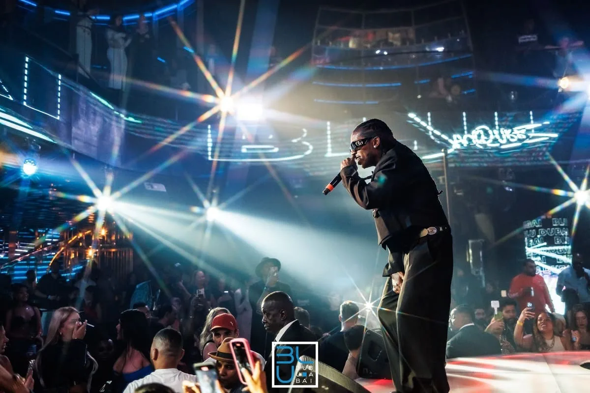 Artist performing on stage at BLU Dubai under starburst lights, with the BLU sign glowing behind the crowd