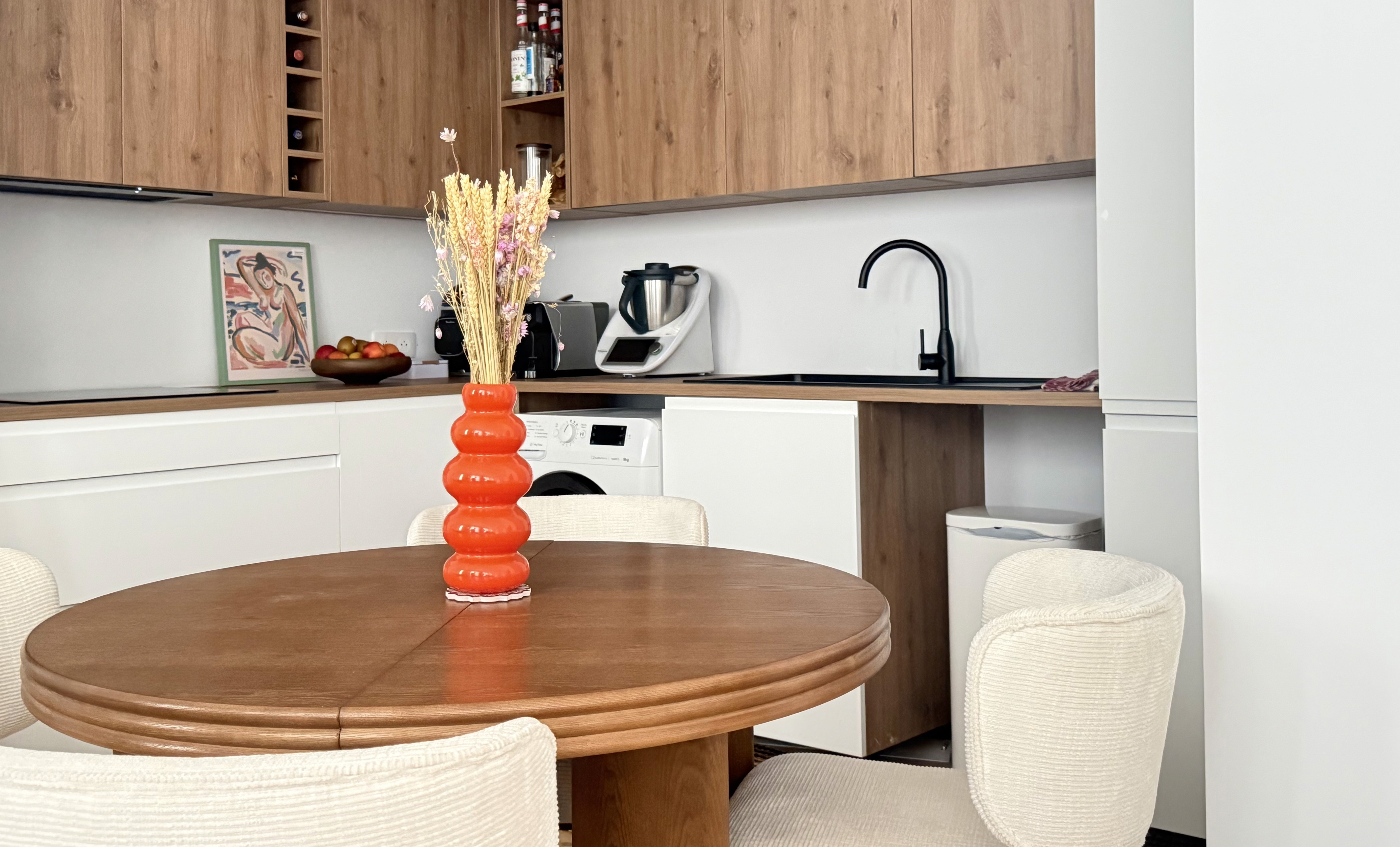 Cuisine moderne optimisée avec meubles en bois et blanc, table ronde de salle à manger et intégration discrète de l'électroménager.