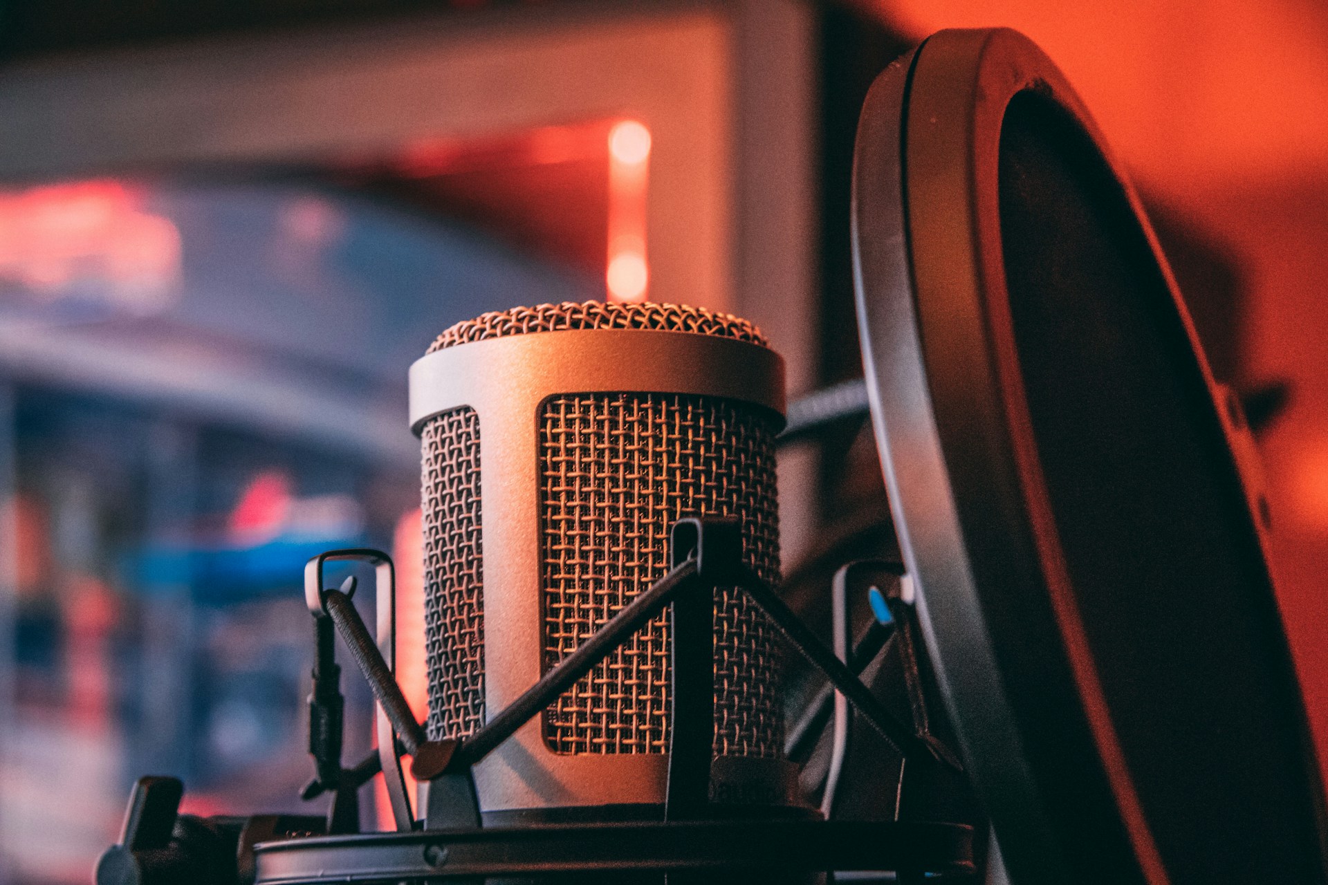 A studio-style condenser microphone with a pop filter is positioned close-up under warm, orange lighting, likely for recording vocals or instruments.