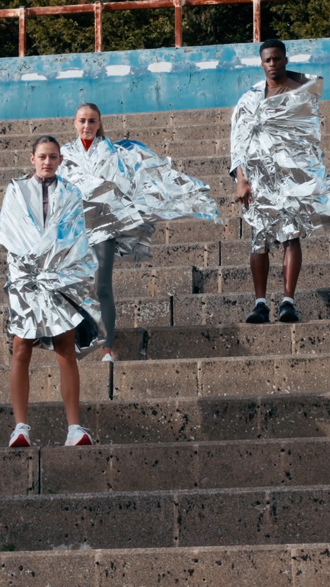 Bride sitting on ground against wall, groom standing nearby