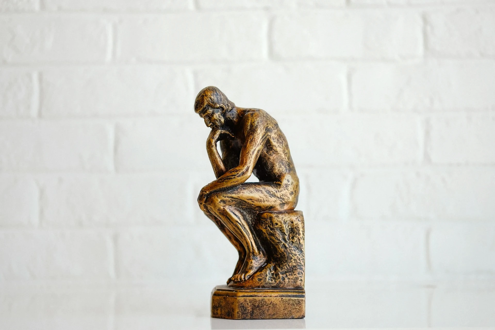 Golden statue of a seated figure in a thoughtful pose, symbolizing deep contemplation and philosophical inquiry.
