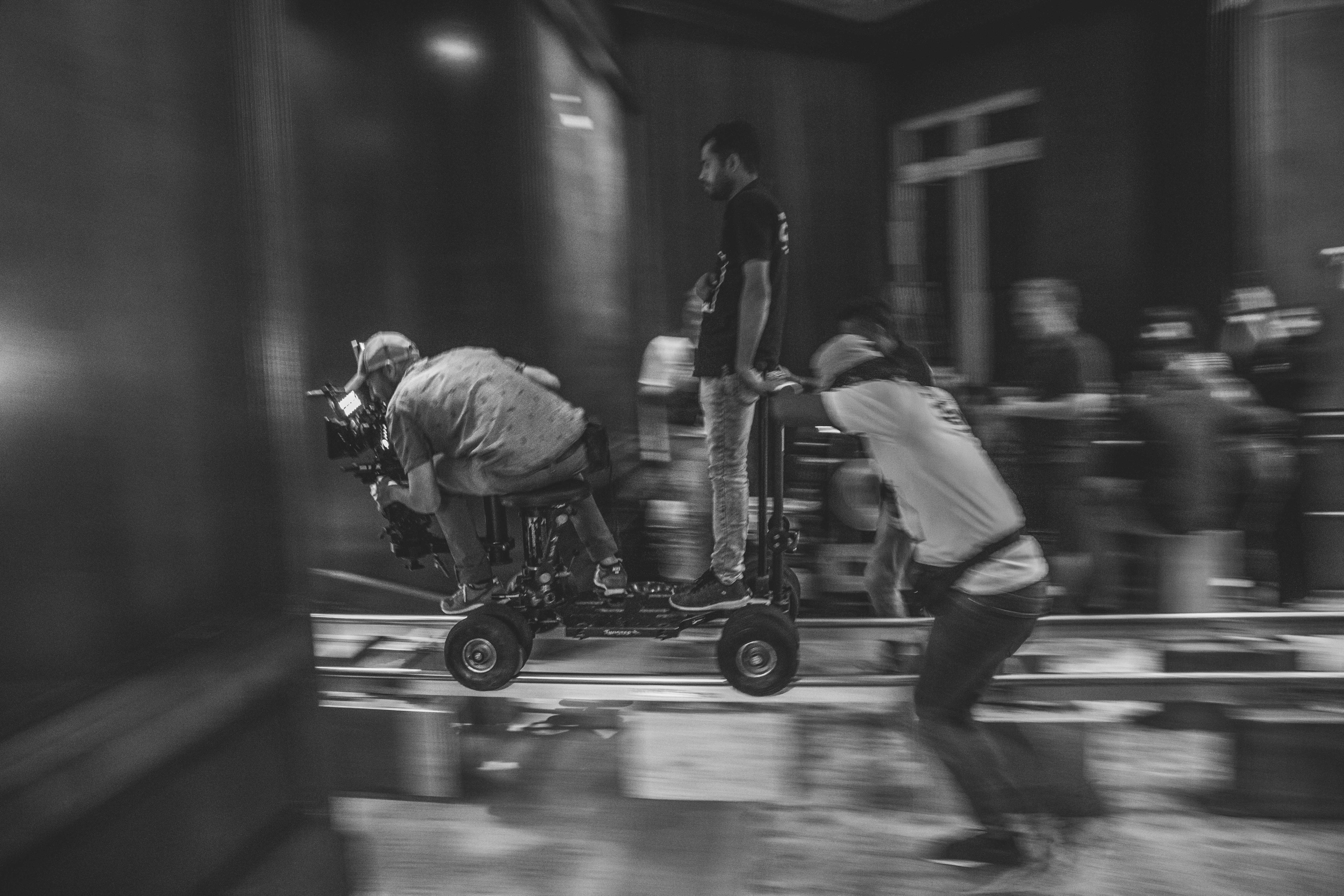 Black and white image of people working at a table with laptops, showing hands gesturing during discussion of digital content displayed on screens, with fabrica® logo in the corner.