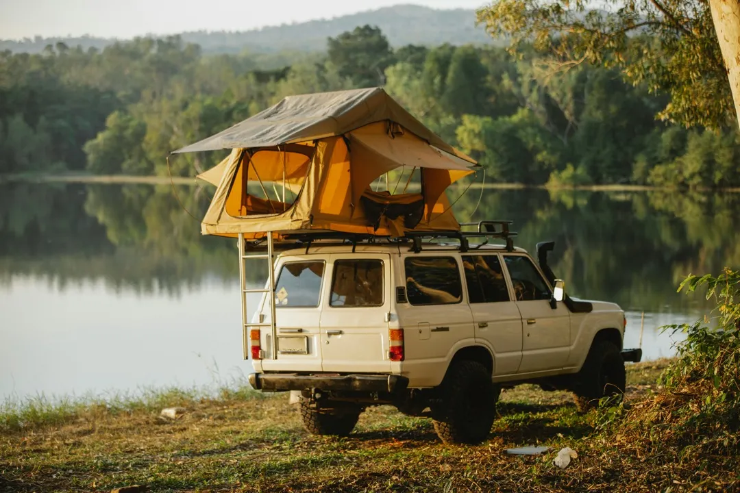 four wheel drive vehicle set up with a rooftop tent next to a lake at golden hour