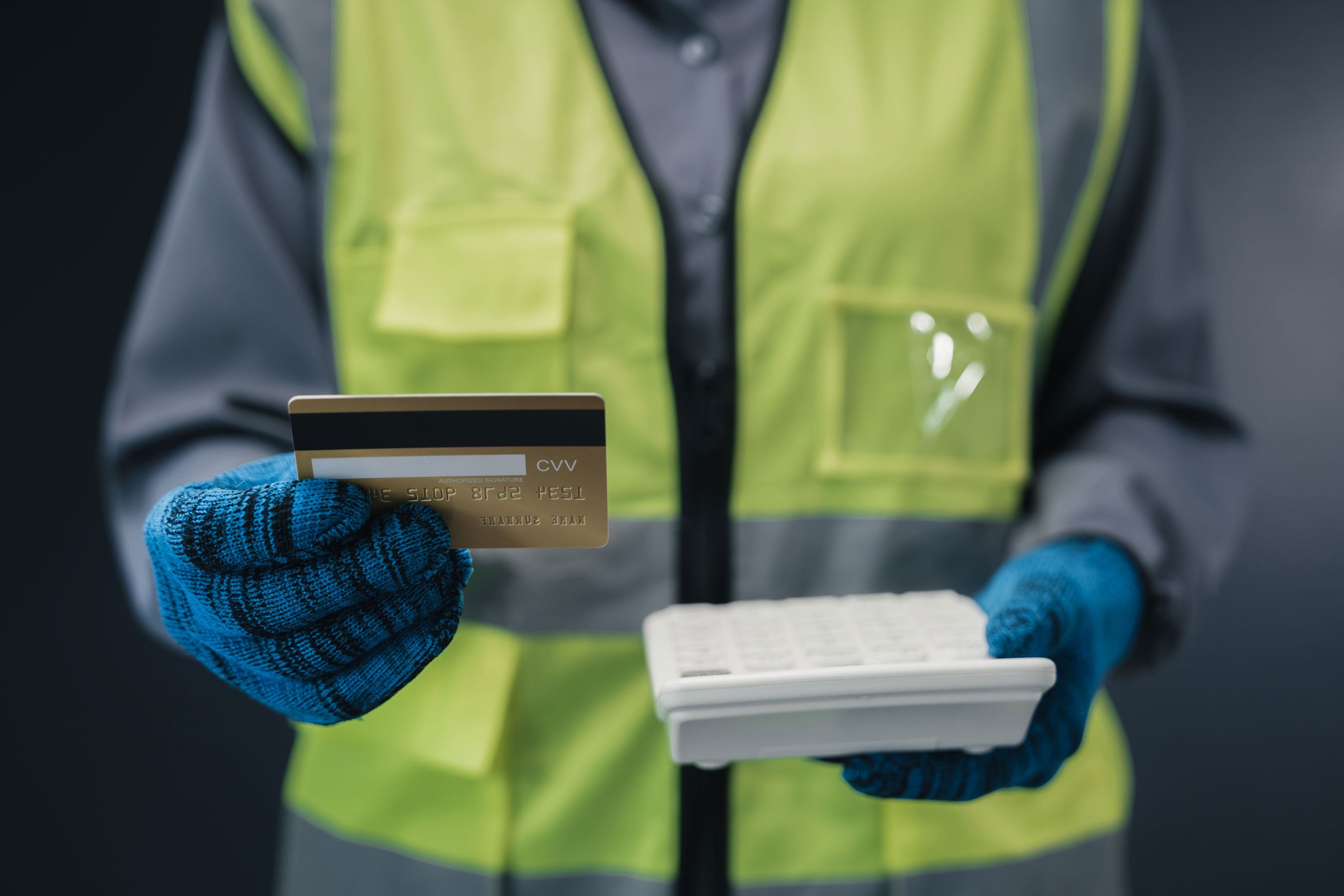 Worker wearing a yellow high-visibility jacket, holding a payment card and a calculator.