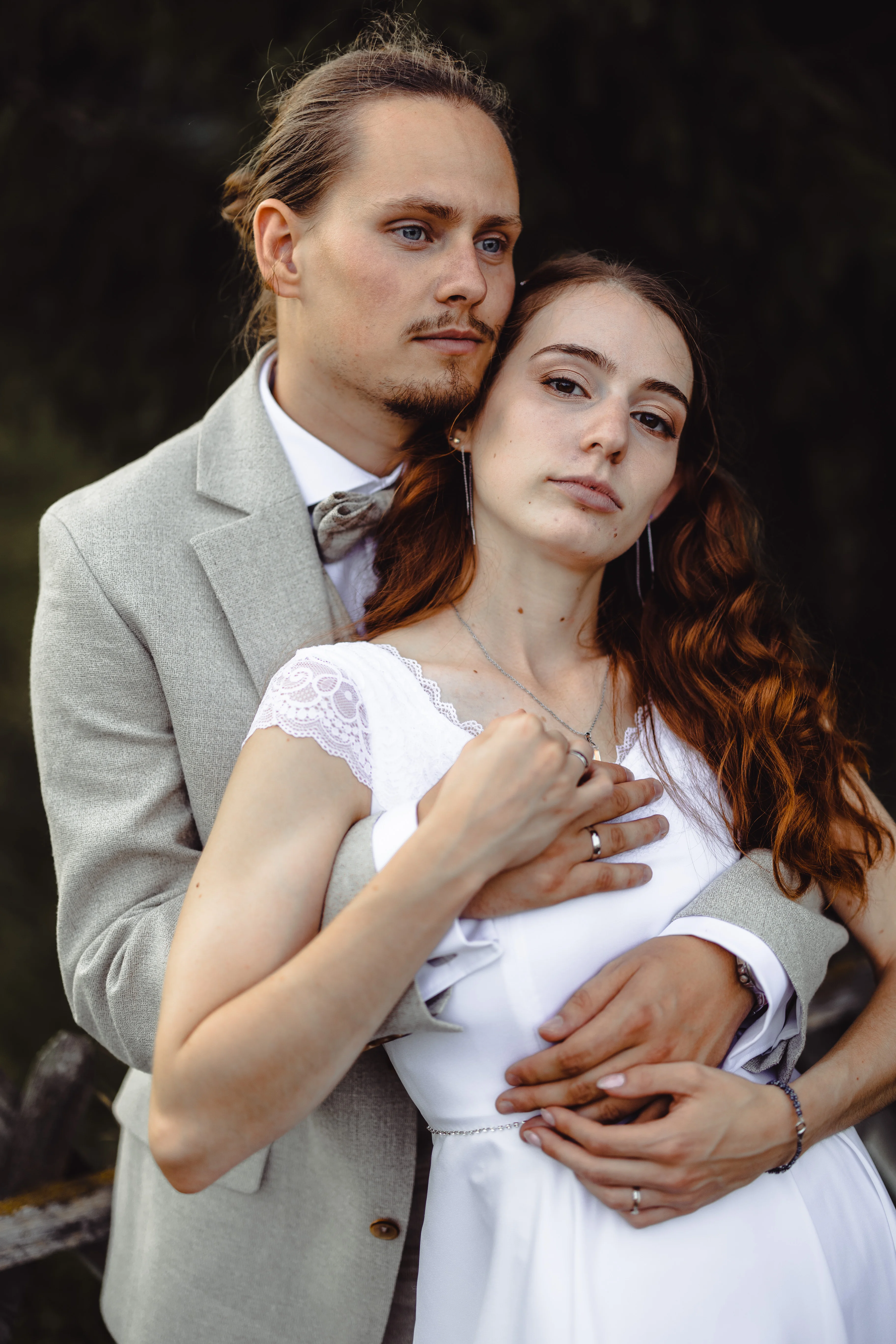Romantikus esküvői portré: vörös hajú menyasszony fehér csipkés ruhában és vőlegény világos öltönyben ölelkezve, természetes fényben Hatvanban