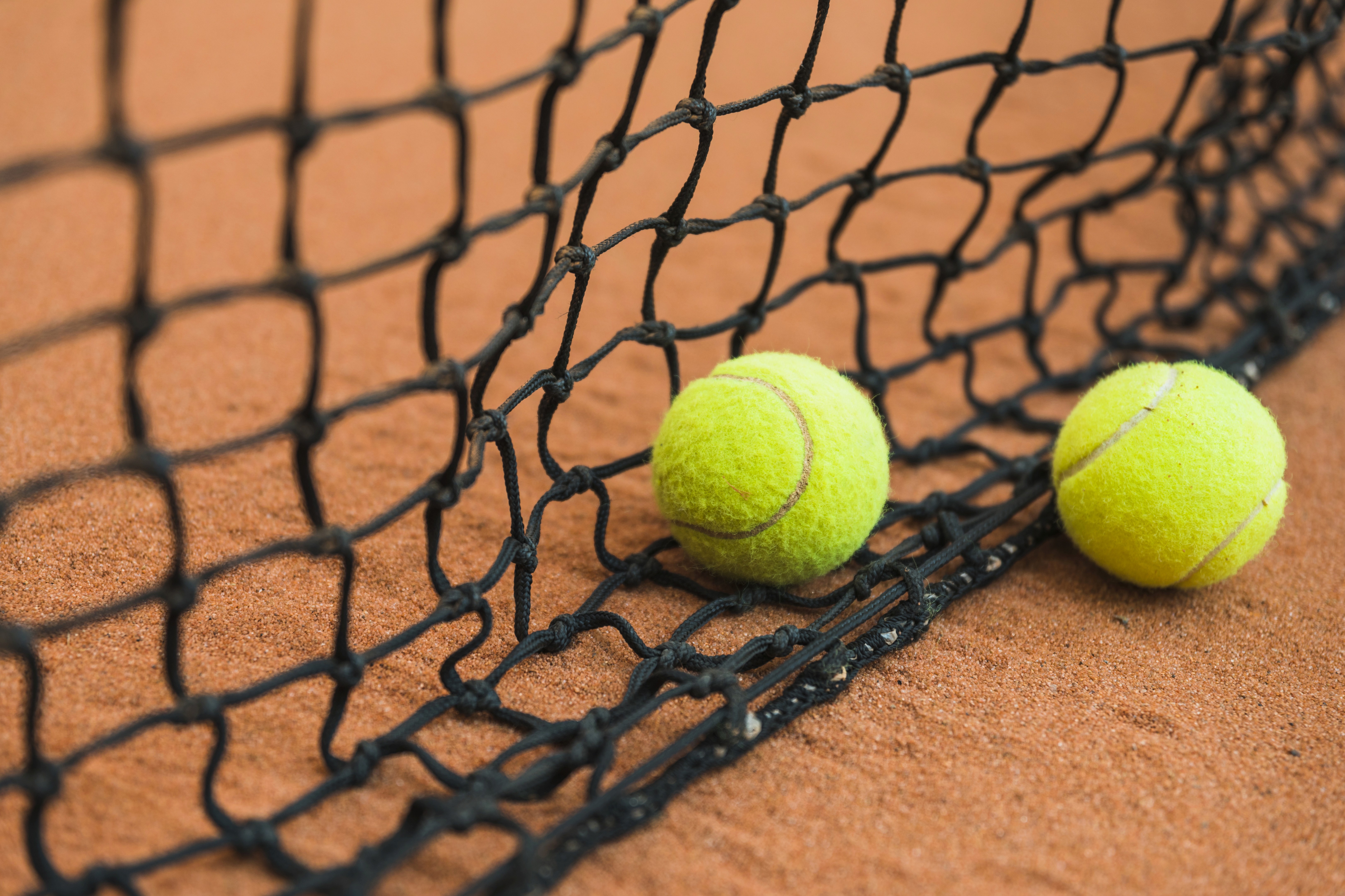 Two tennis balls on the net of a clay court