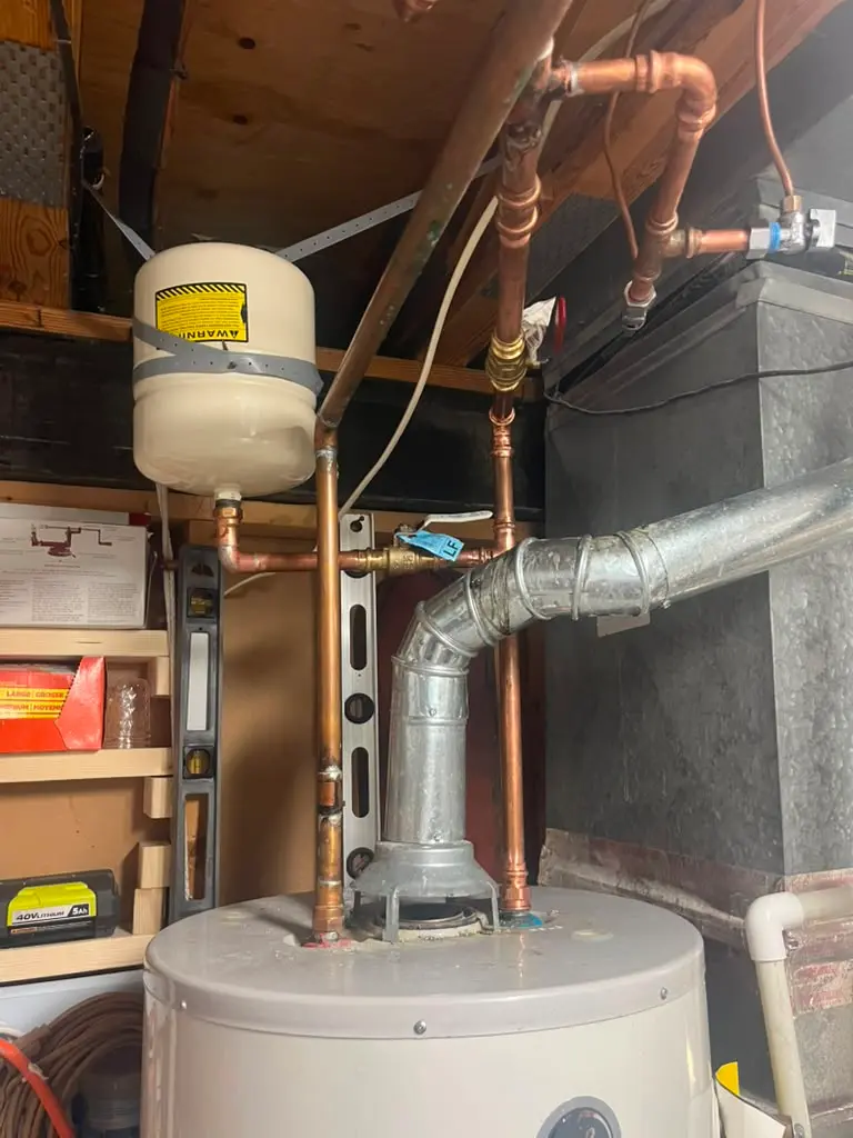 A professional water heater installation featuring new copper piping, a shutoff valve, and an expansion tank installation.
