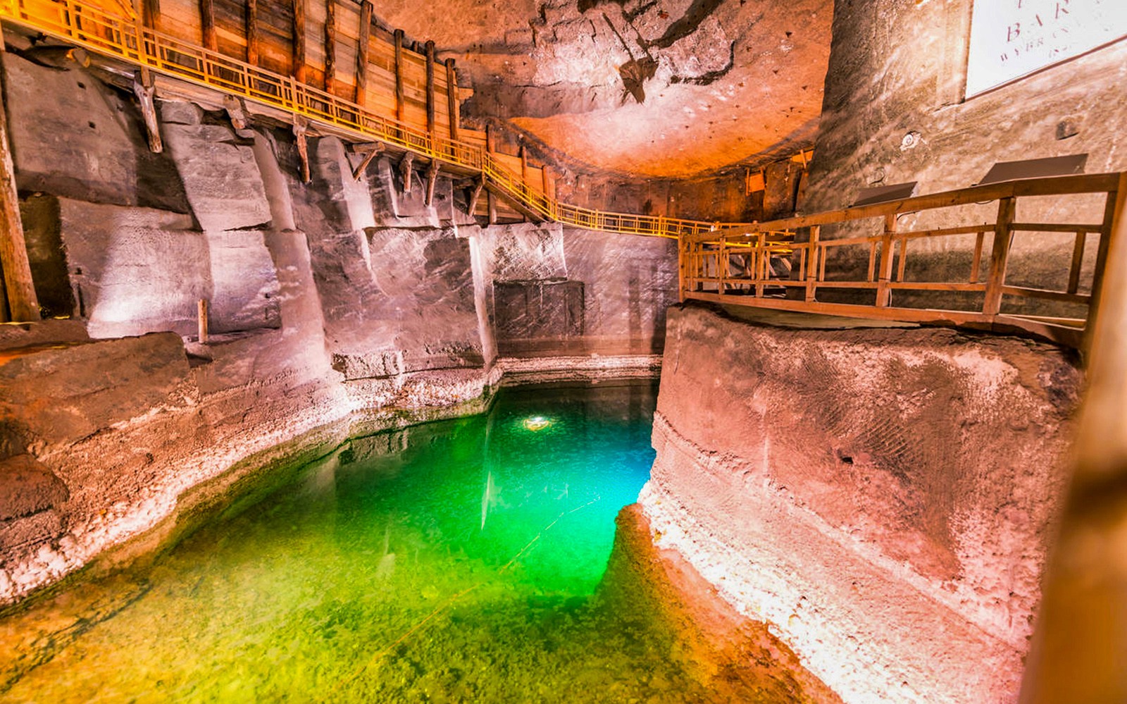 Cámara de la Mina de Sal de Wieliczka con pasarelas de madera y agua verde iluminada.