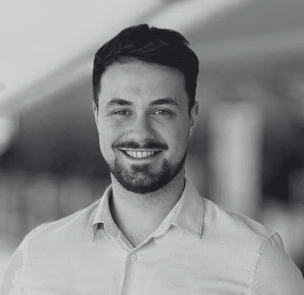 Portrait of a man with short dark hair and a trimmed beard, dressed in a dark shirt, on a simple background.