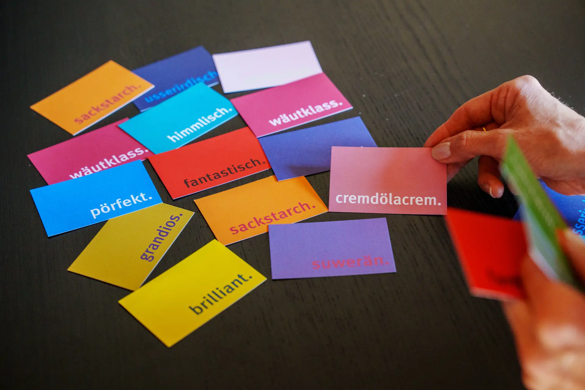 Farbige Moderationskärtchen mit Dialekt-Begriffen wie „wäutklass“ und „grandios“ auf einem Tisch.
