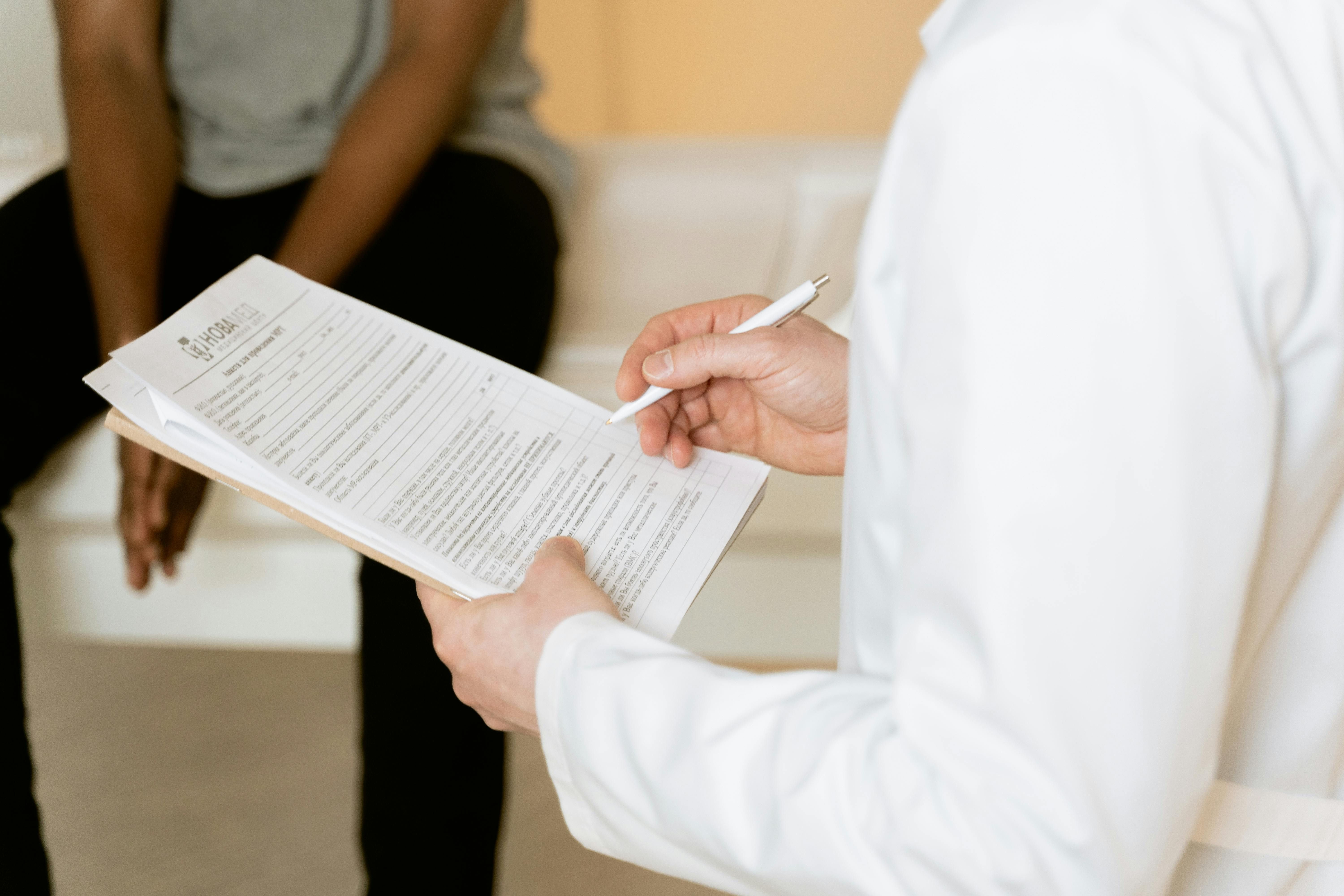 Doctor in white coat writing on clipboard during patient consultation.