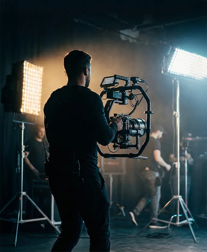 A woman with curly red hair, wearing a white top, lace skirt, and brown boots, walks while carrying a large bouquet of sunflowers over her shoulder.