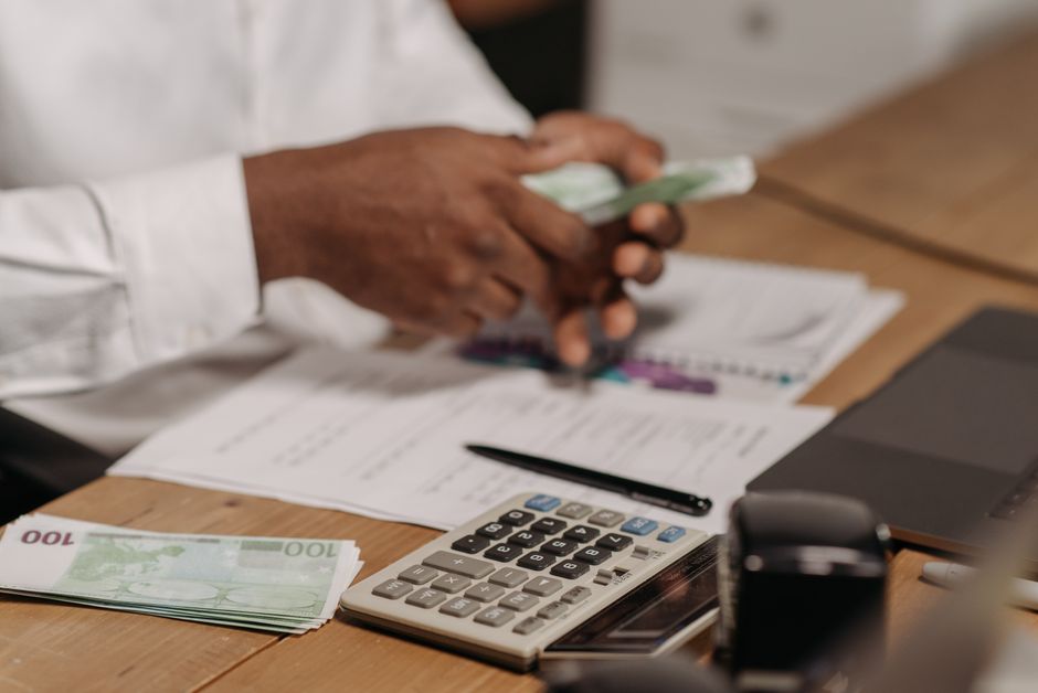 Mâini care numără bani lângă calculator și laptop, sugerând că împrumutul de la fondator se face doar prin bancă, nu cu numerar