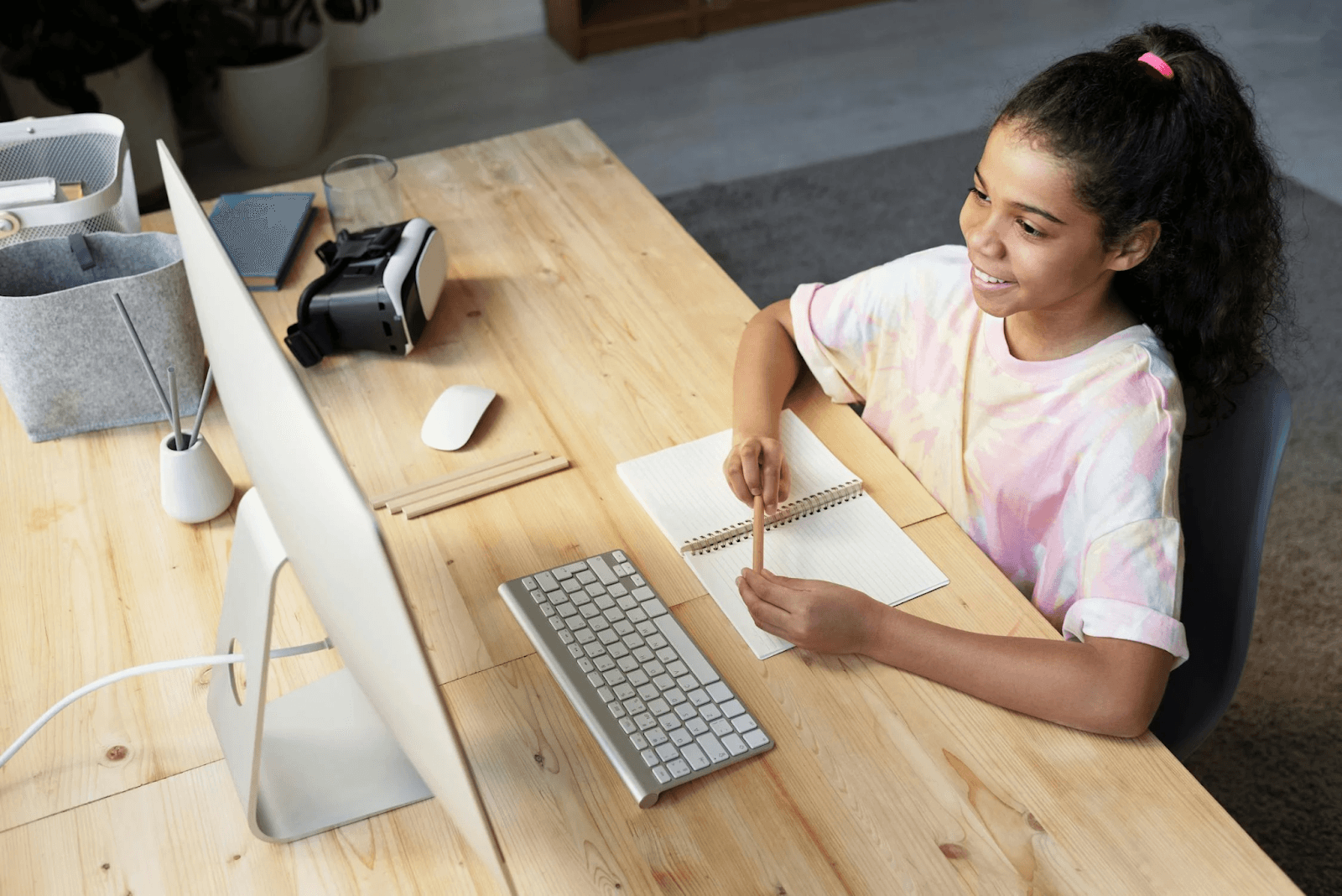 A girl with a pen and notebook looking at an iMac 