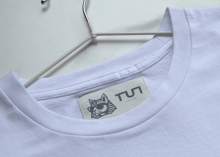 TUT Designs neck label on white t-shirt, featuring pharaonic cat logo and modern Egyptian fashion brand identity.