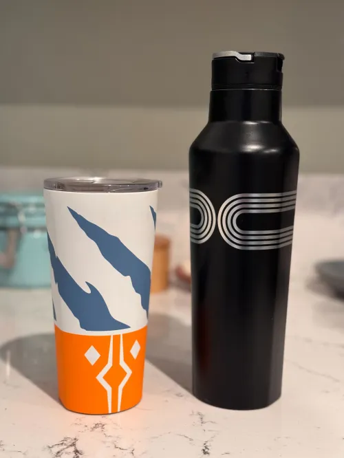 A Corkcicle tumbler with an Ahsoka Tano tumbler next to a Corkcicle water bottle with a Kylo Ren design. Both are on a white marble countertop