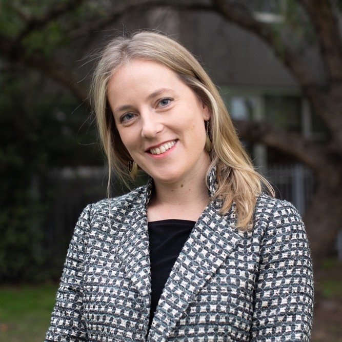 A portrait of Helen Osborne, the founder of Ground Truth. Smiling woman with long hair wearing a patterned blazer, standing outdoors with trees in the background.