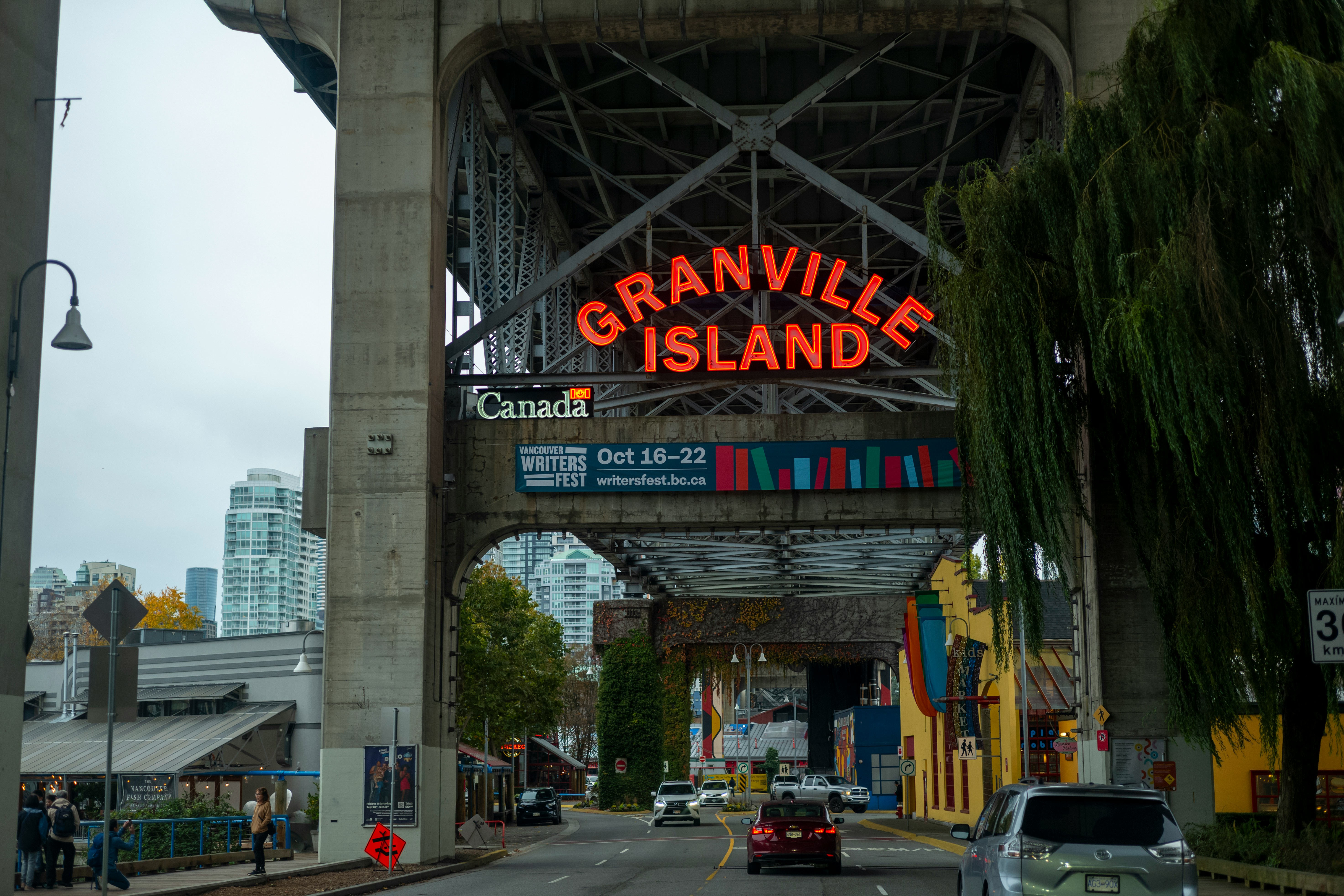 A road runs beneath a bridge with a neon sign "Granville Island" above