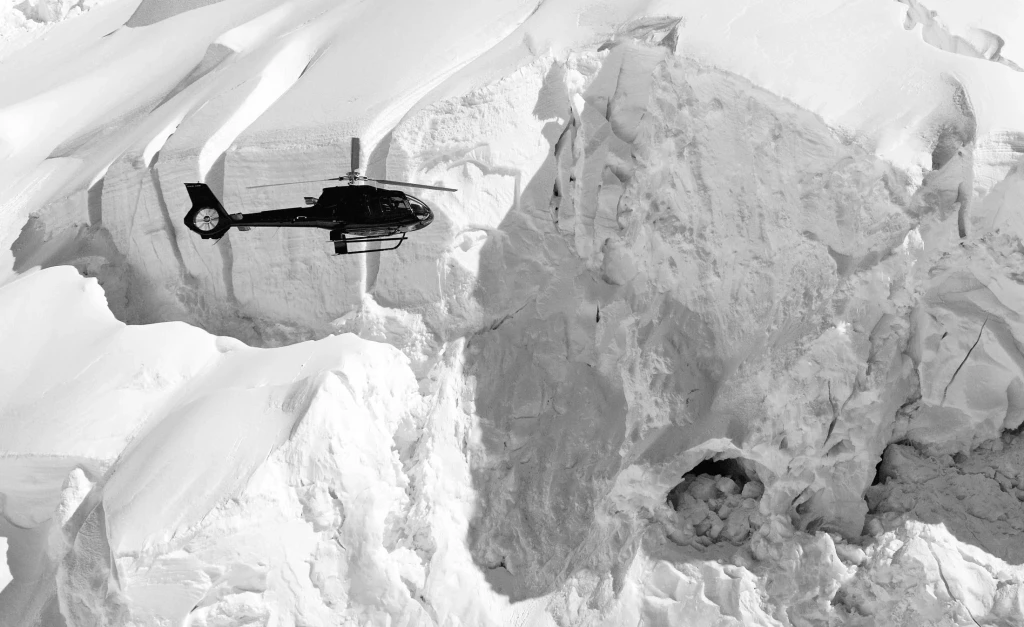 A helicopter flying over a rugged snow-covered mountain landscape