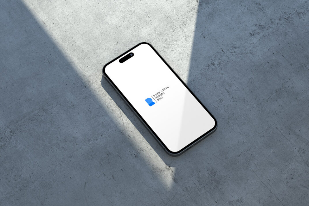 Minimalist smartphone mockup featuring a black frame device placed on a concrete surface under angled natural lighting, creating bold shadows. The screen displays a placeholder design.