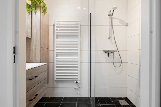 De badkamer met een glazen douchewand, een handdoekradiator en witte wandtegels.