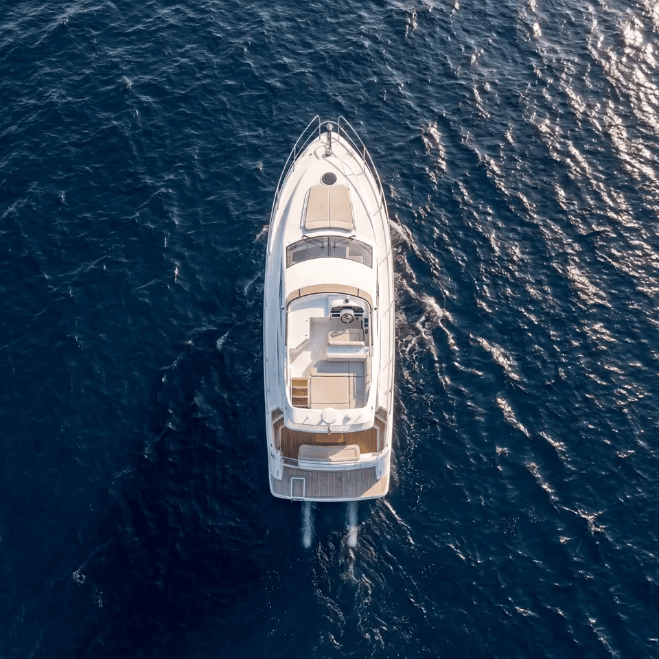 Overhead night aerial photograph of a Beneteau Clipper 361 sailing yacht with warm interior cabin lighting illuminating the teak deck, set against a dark black ocean background