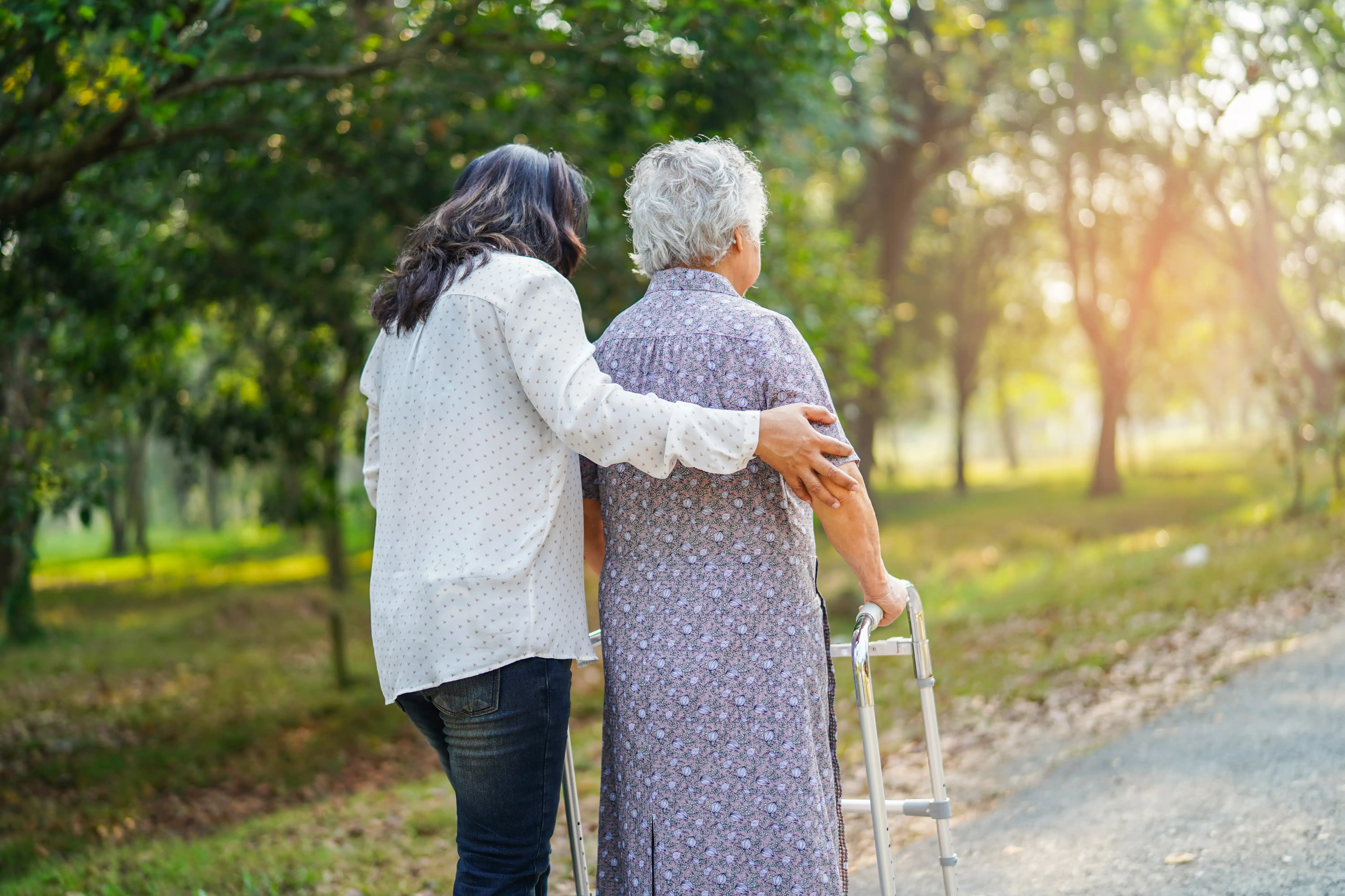 An adult daughter helping an elderly woman walk with a walker outdoors, illustrating family care leave rights under California's CFRA