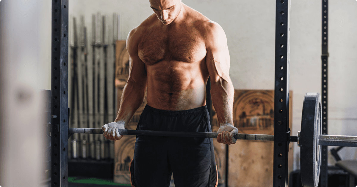 A muscular man in a gym, holding a barbell at the bottom of the movement, 