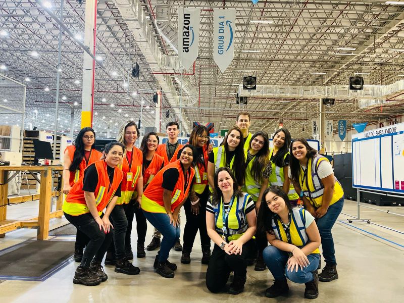 Amazon fulfillment center diverse team of warehouse employees in safety vests showcasing inclusive workplace culture, gender diversity, and collaborative team environment in modern logistics facility - employer branding campaign emphasizing inclusivity, team spirit, and growth opportunities following reputational crisis, strategic repositioning by Alessandro Brancati Marketing & Growth Studio via Adecco