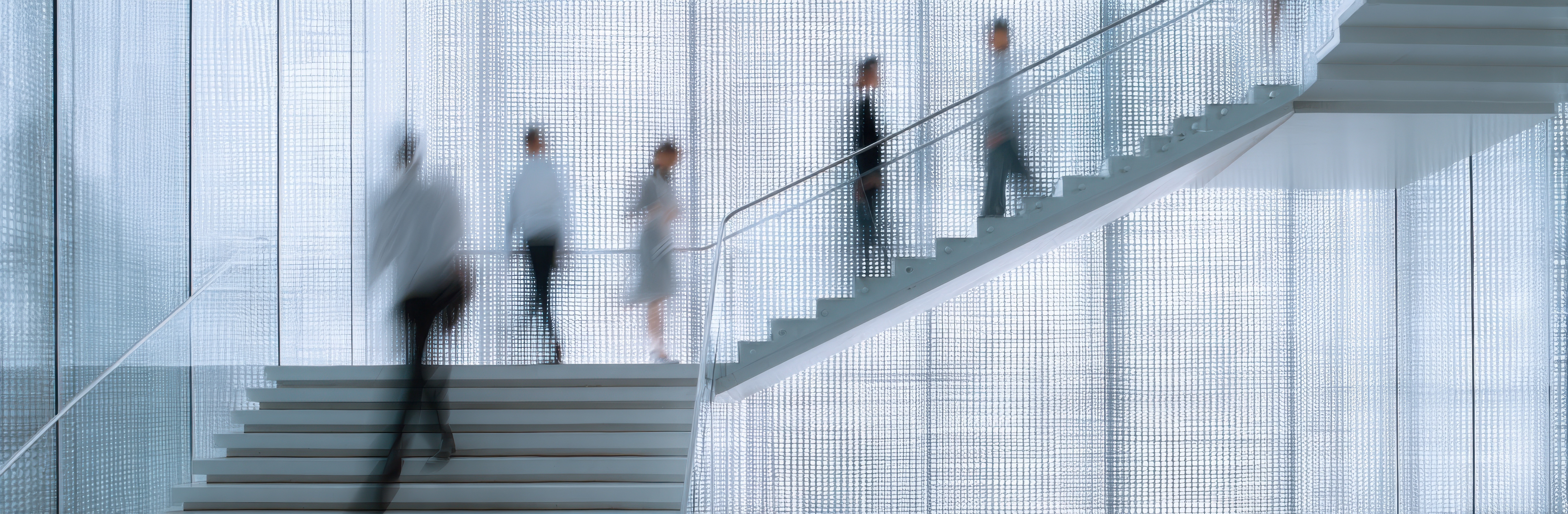 Geschäftsleute, die eine moderne Treppe in einem Bürogebäude hinaufgehen, symbolisieren ein strukturiertes Richtlinienmanagement, klare Governance und einen kontrollierten Richtlinienlebenszyklus innerhalb der Organisation.