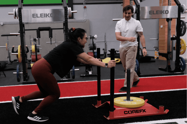 Patient pushing a sled supervised by a physiotherapist on a gym turf