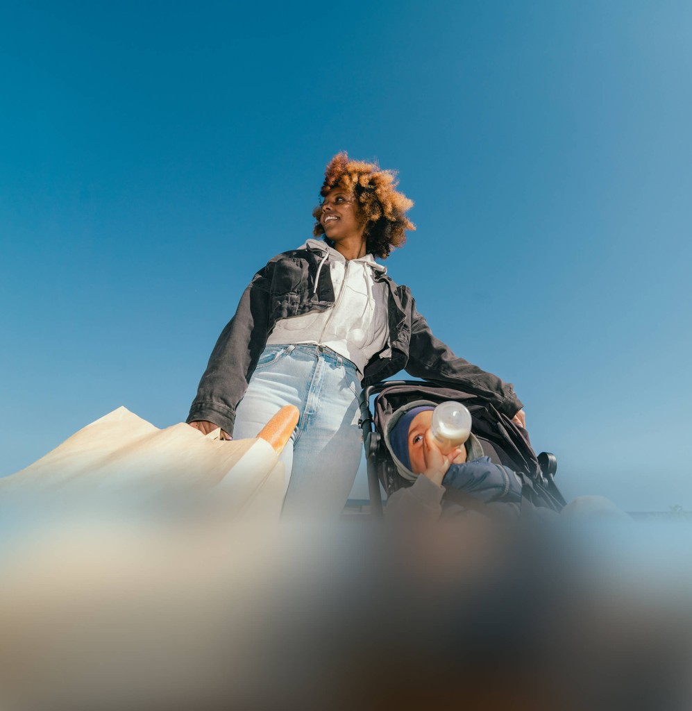 A mother and her toddler against a clear blue sky, wearing casual clothing and looking confidently ahead.