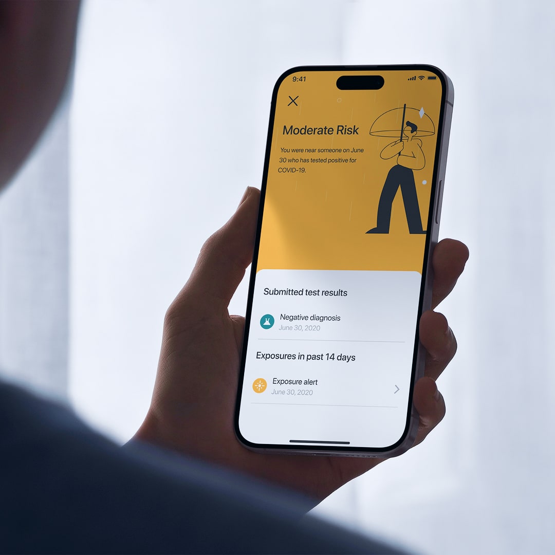 Hand holding smartphone displaying PWC Zone Check app with moderate risk alert, negative diagnosis result, and exposure alert