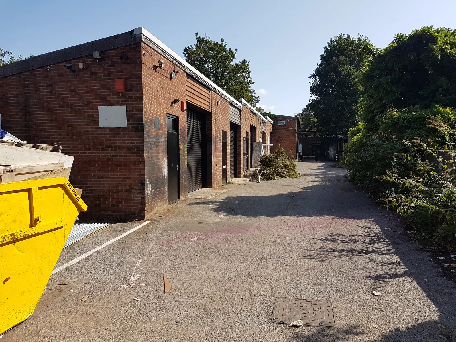 Narrow alleyway with brick buildings on one side and a yellow dumpster on the other, under clear blue skies.