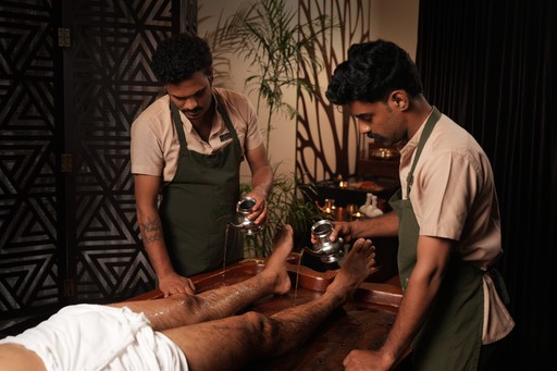 Ayurvedic therapy for skin diseases – Two therapists performing an oil-pouring treatment on a guest’s legs, promoting skin rejuvenation and holistic healing in a serene wellness setting at au revoir resort 