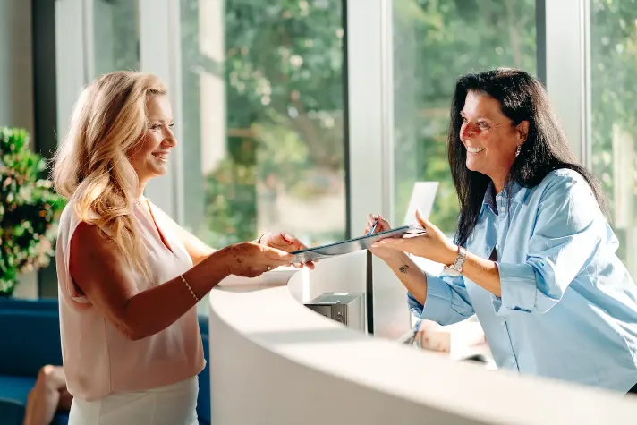 Idősebb férfi és fiatalabb nő kezet fognak egy recepciónál, háttérben orchideával.