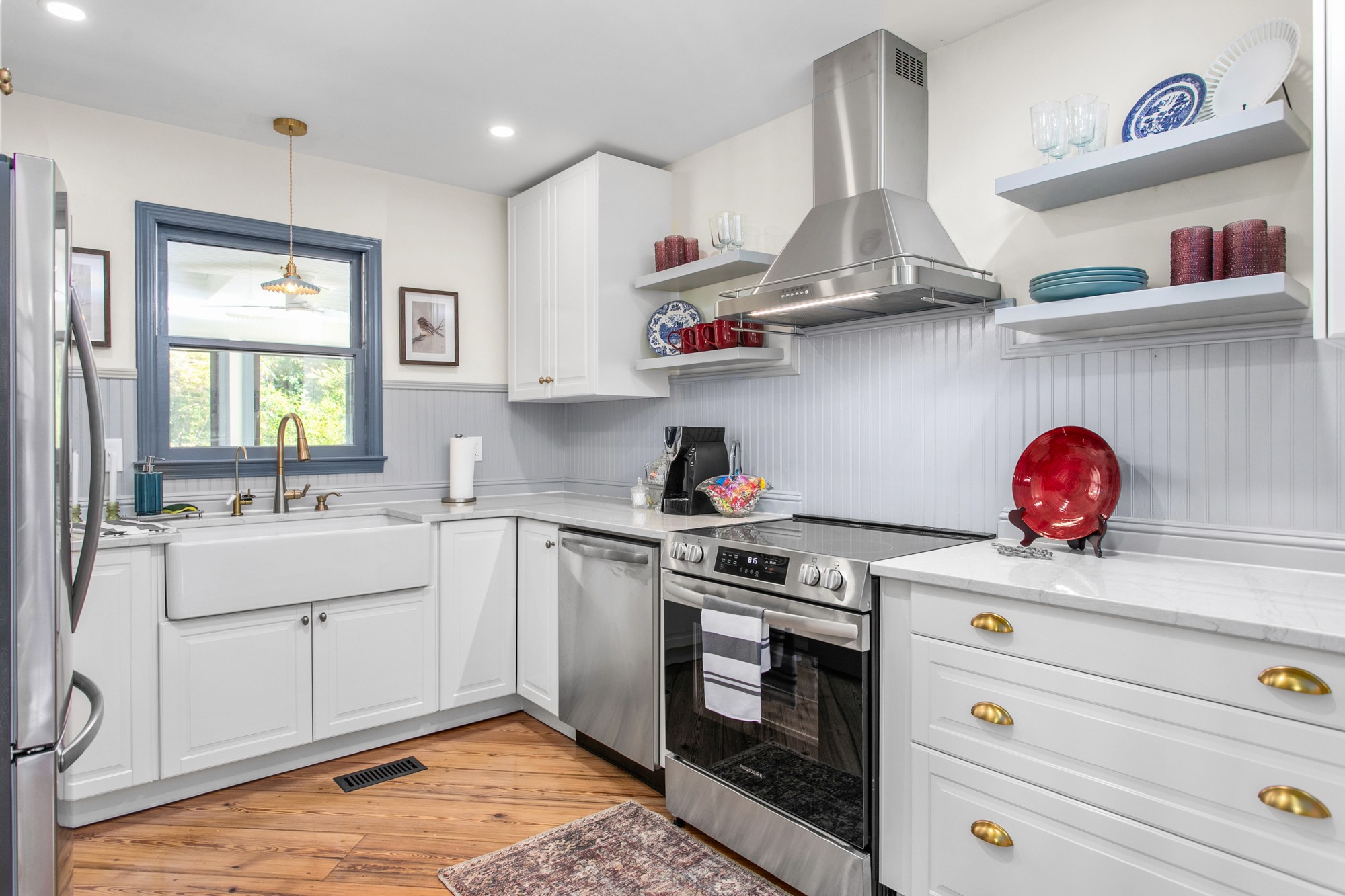 Updated white Airbnb kitchen with brass hardware, open shelving, island seating, and blue-gray details