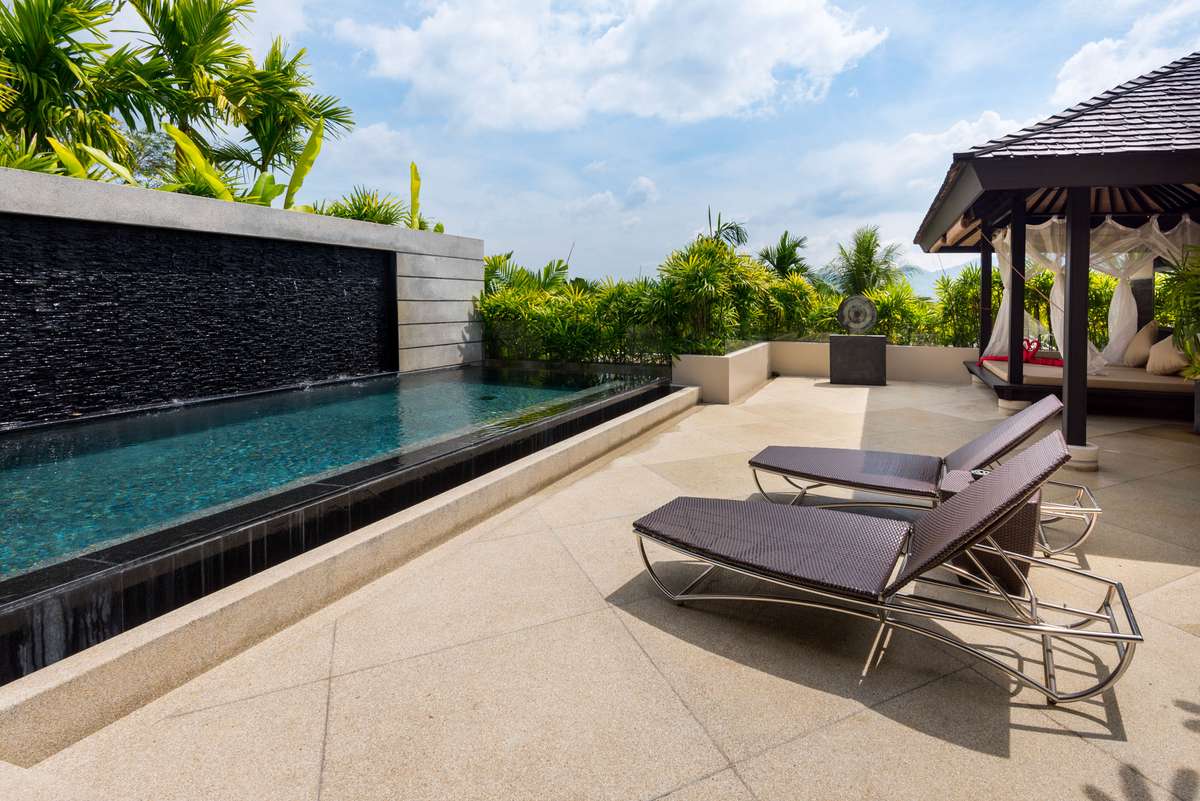 A private infinity pool with dark tile walls and a stone deck features two lounge chairs under a thatched roof pavilion.