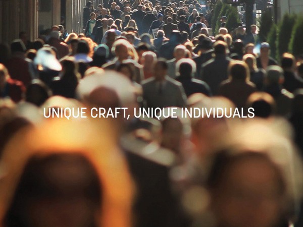 The image depicts a large crowd of people moving along a city street. The individuals are out of focus, creating a sense of depth and distance. The scene is captured from a slightly elevated angle, looking down at the crowd. The text "UNIQUE CRAFT, UNIQUE INDIVIDUALS" is superimposed in white letters across the center of the image.