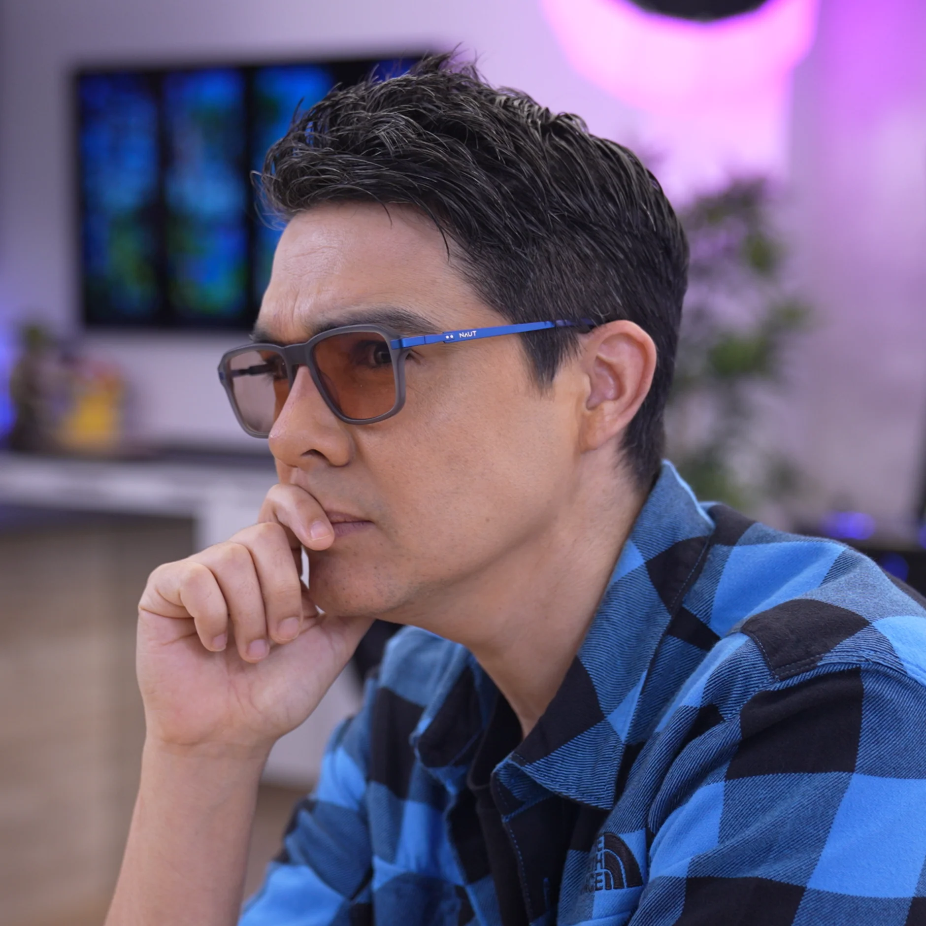 Man dressed in dark casual wear sitting alone in a stadium’s empty rows of purple chairs, lit by dramatic moody lighting.