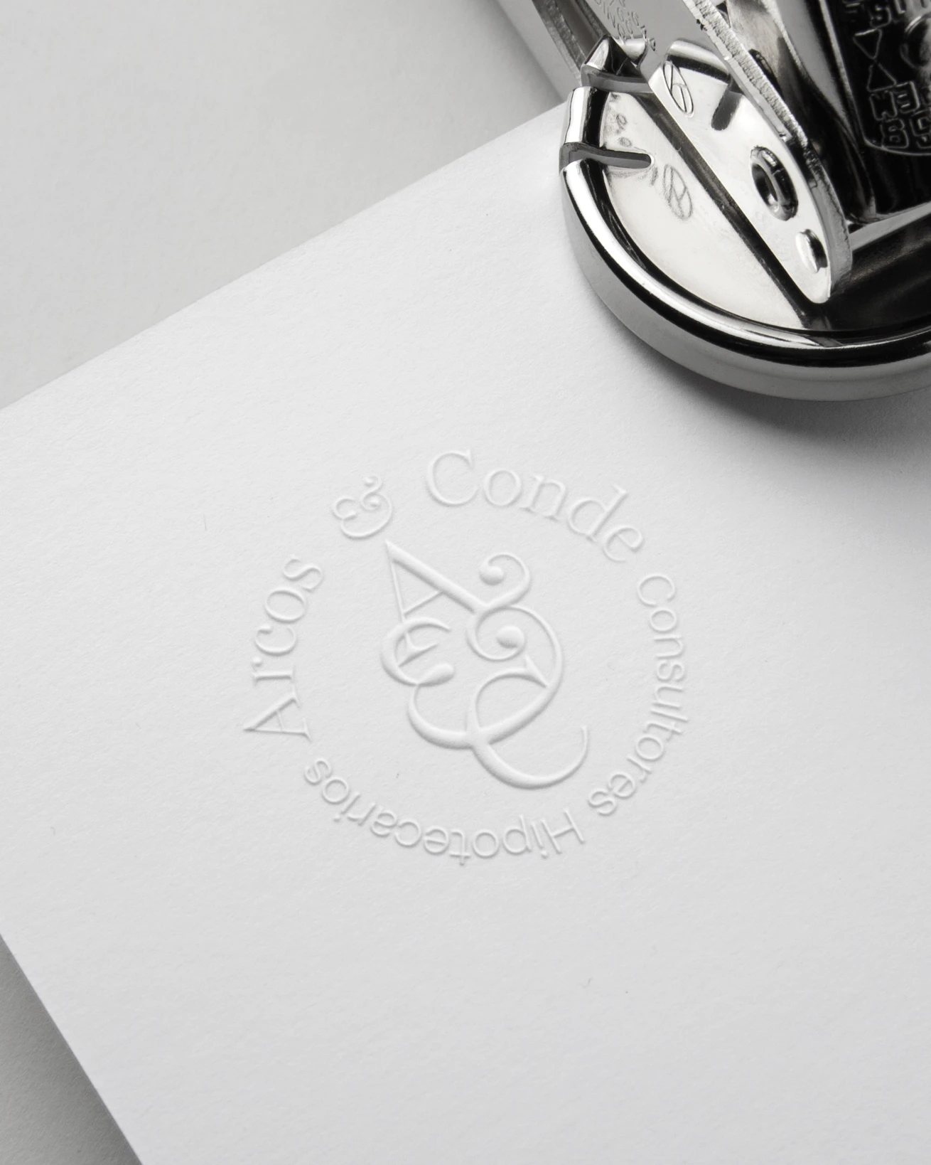 Embossed Arcos & Conde seal on white paper next to a metal embosser, brand identity design by Sebastian Saavedra