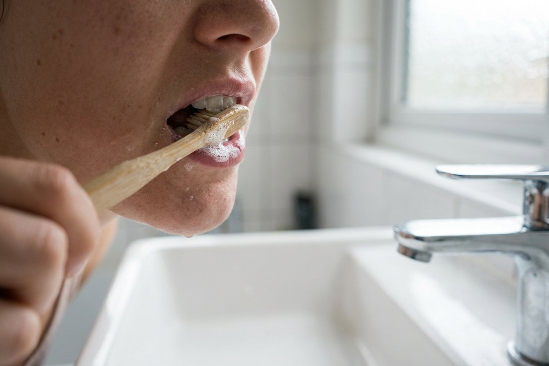 Close-up of a person brushing their teeth at a bright bathroom sink