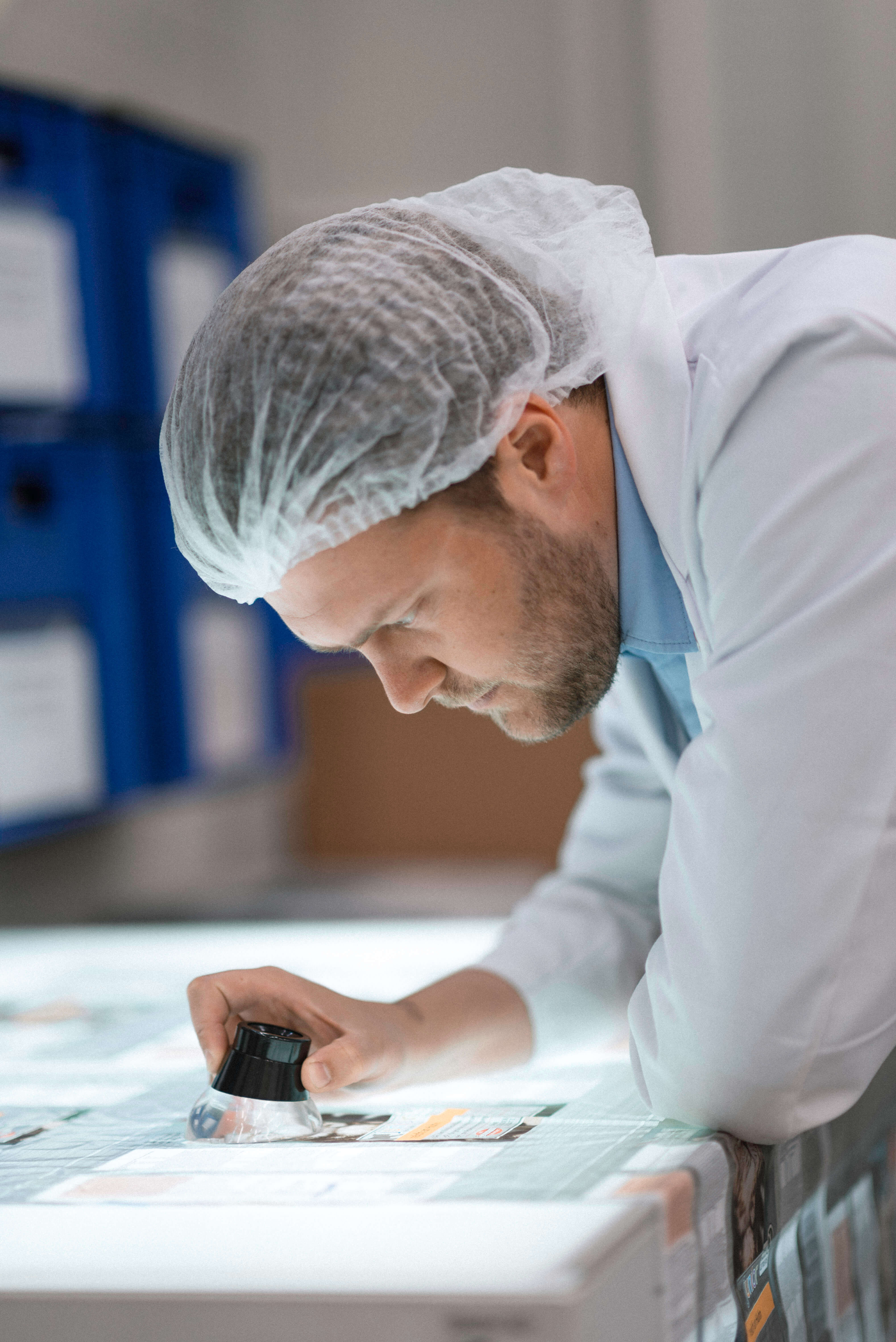 Scheyer member closely inspecting packaging materials on a worktable using a magnifying glass, ensuring detailed quality control.