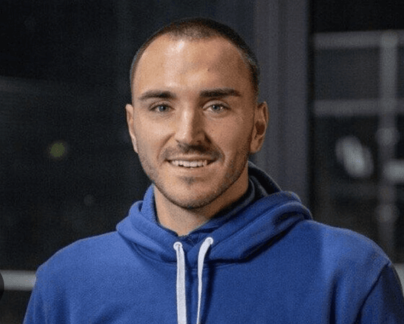 Ein junger Mann mit einem blauen Hoodie in die Kamera lächelnd.