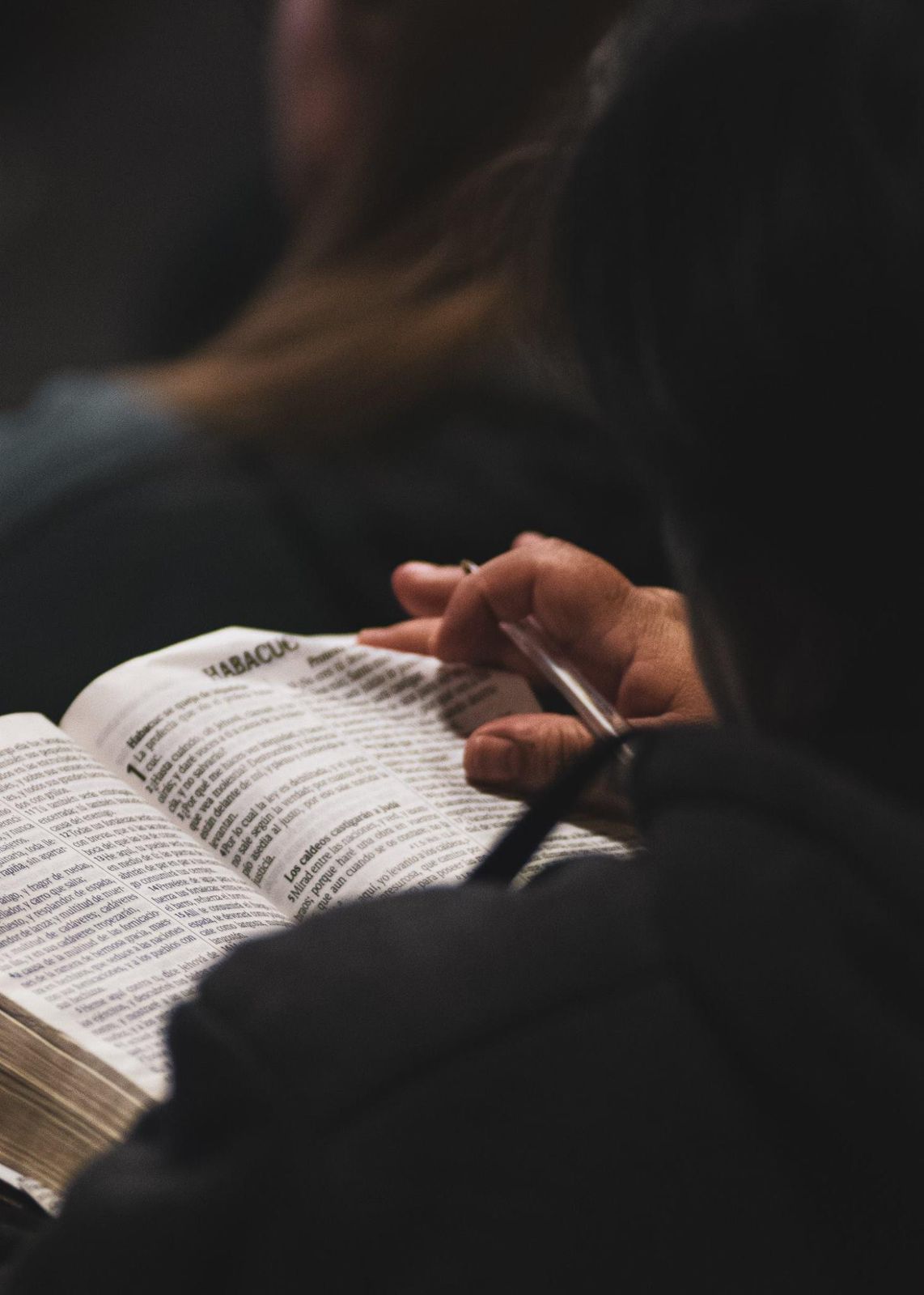 A speaker on stage, illuminated against a dark background, gestures while addressing an audience.