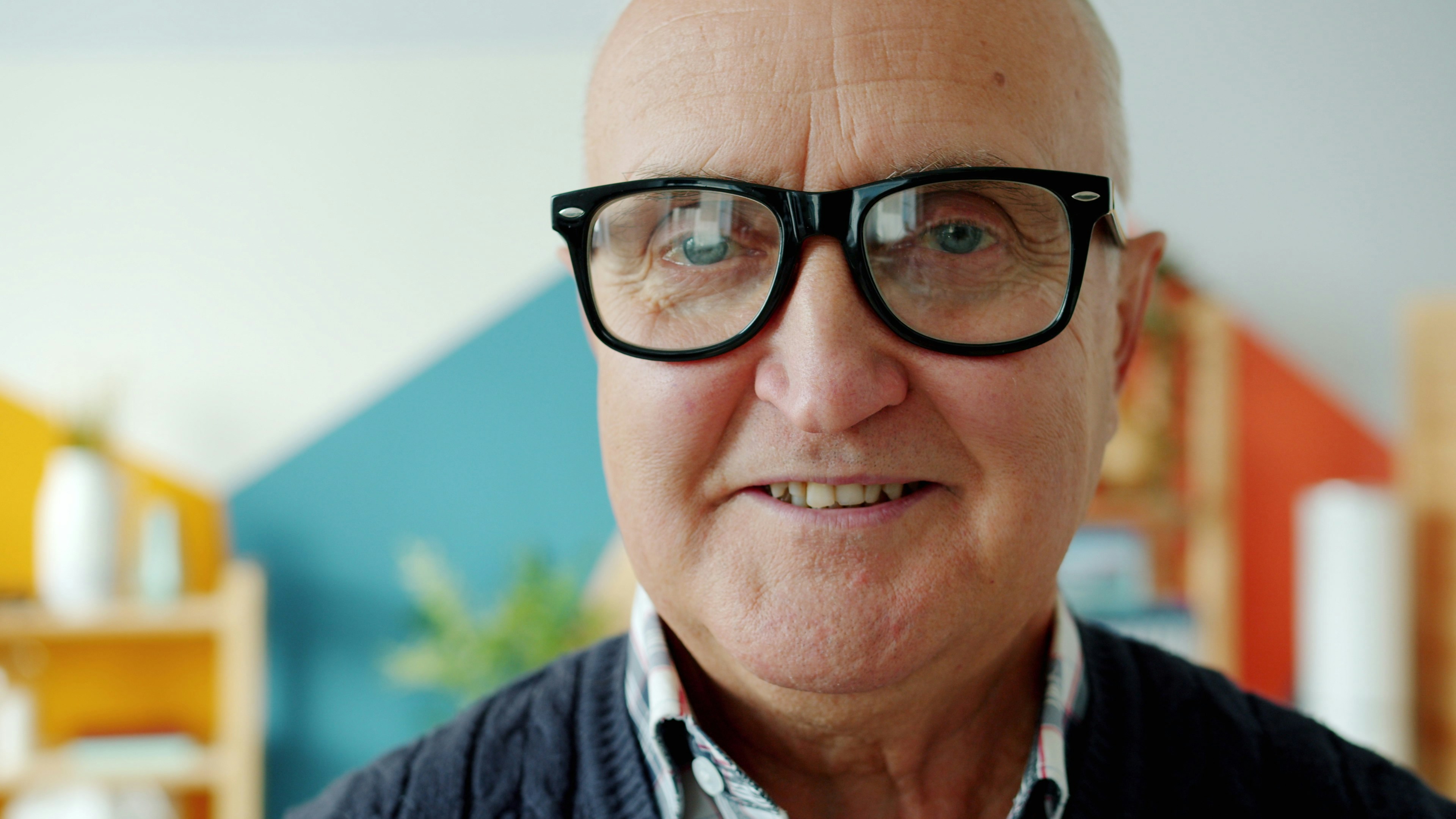 Elderly man with glasses smiling at the camera.